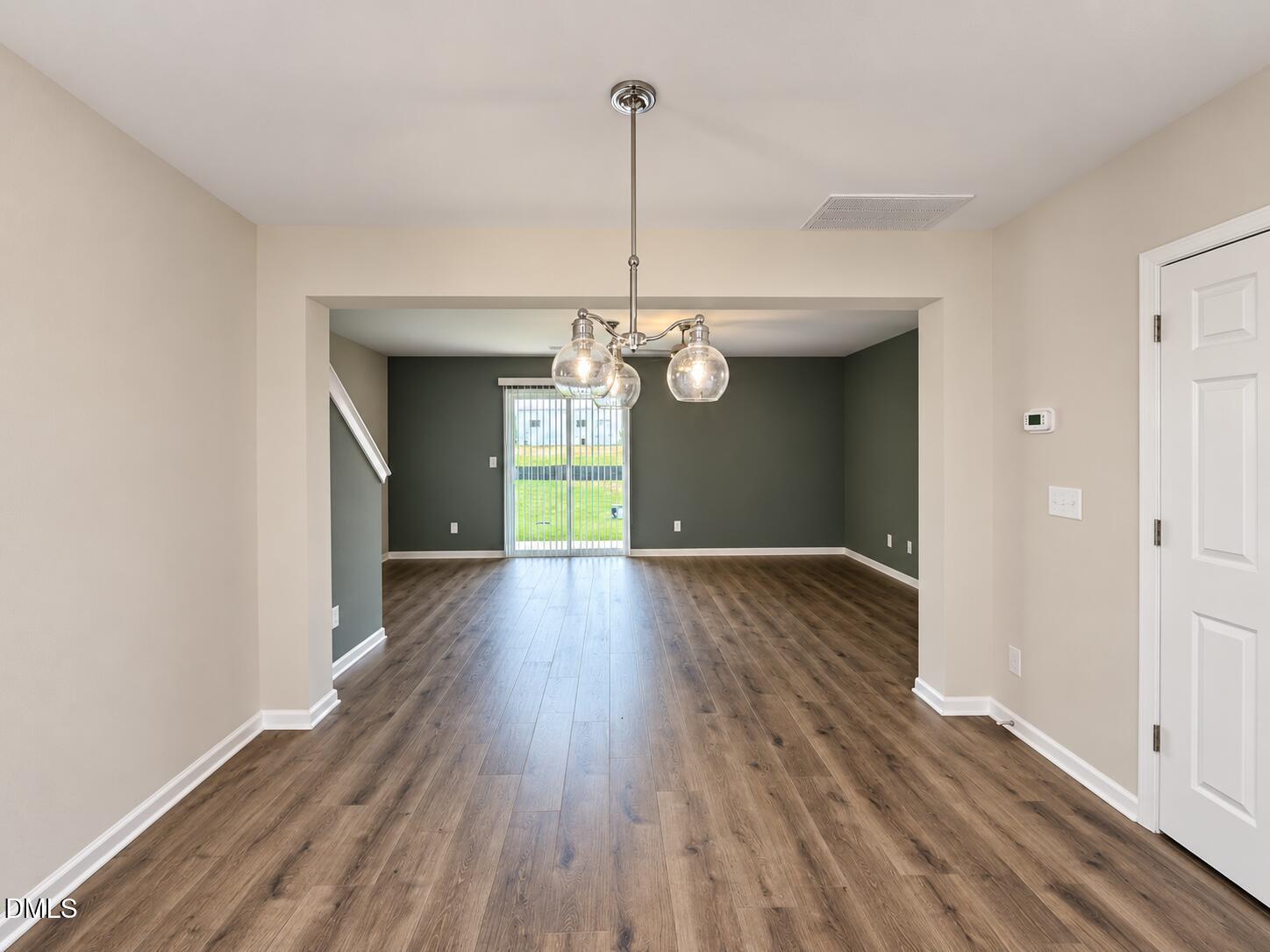 Empty townhome dining area with wood-look floors, a glass-door pendant light, and a dark accent wall.