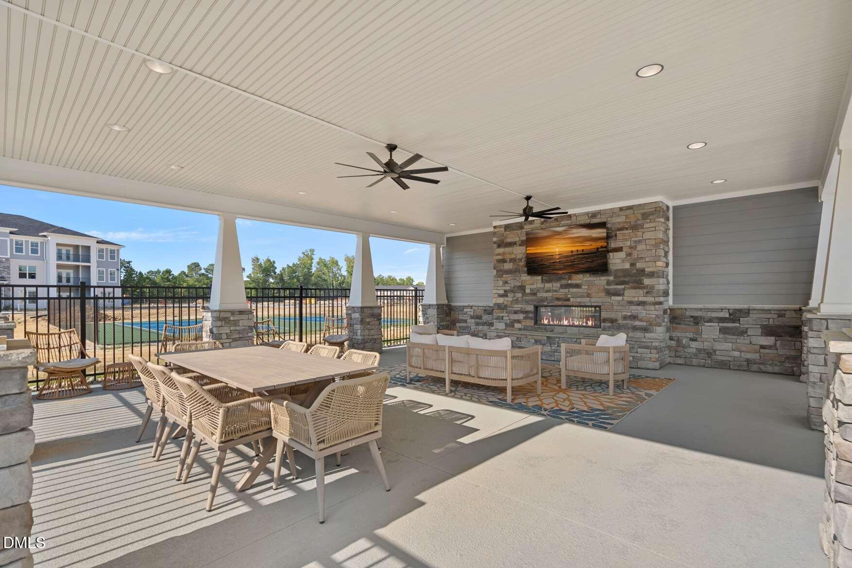 Covered patio with stone fireplace, dining and lounge seating, and a view of the pool.