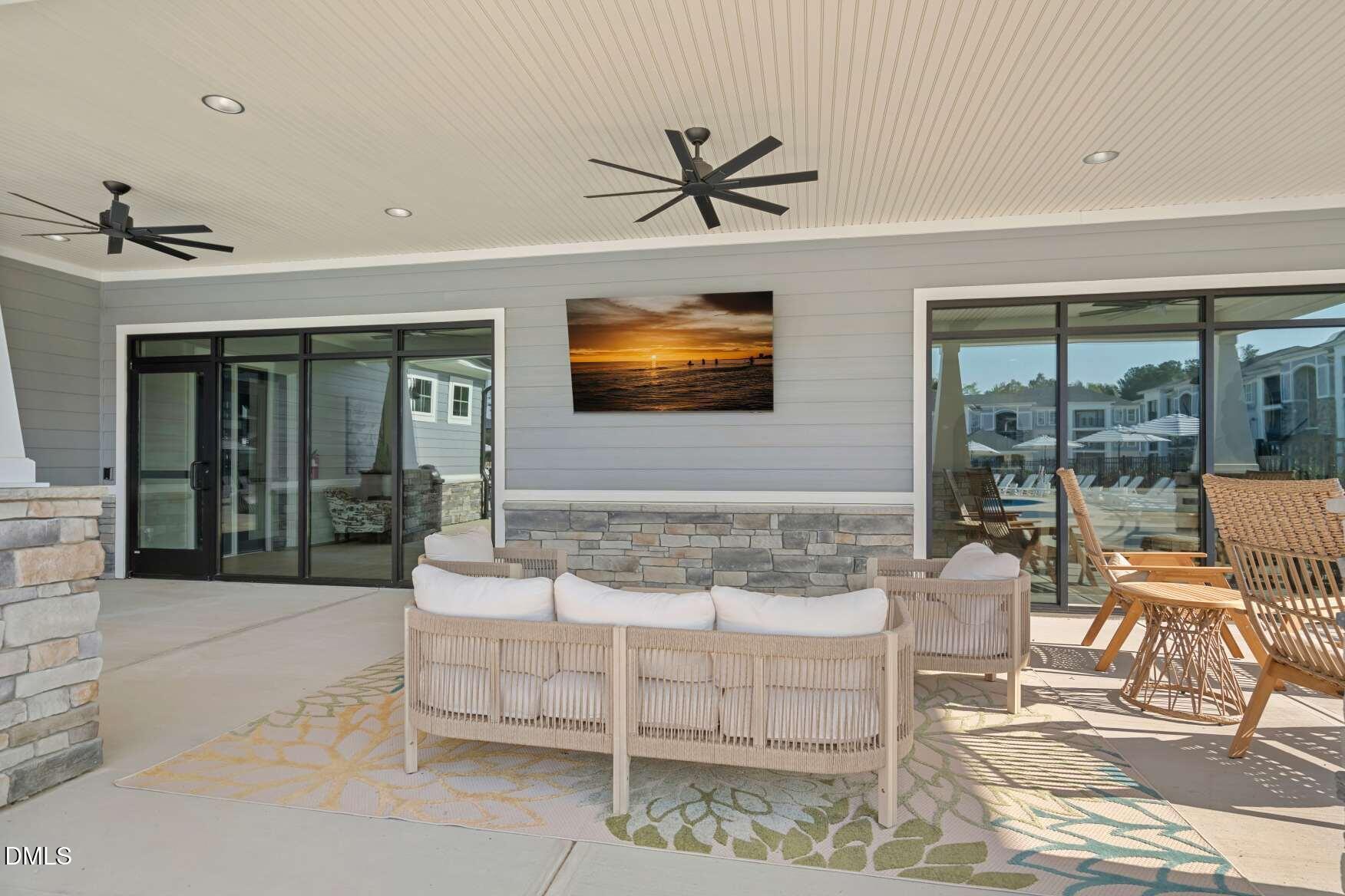 Covered patio with wicker seating, patterned rugs, ceiling fans, and large sliding glass doors.