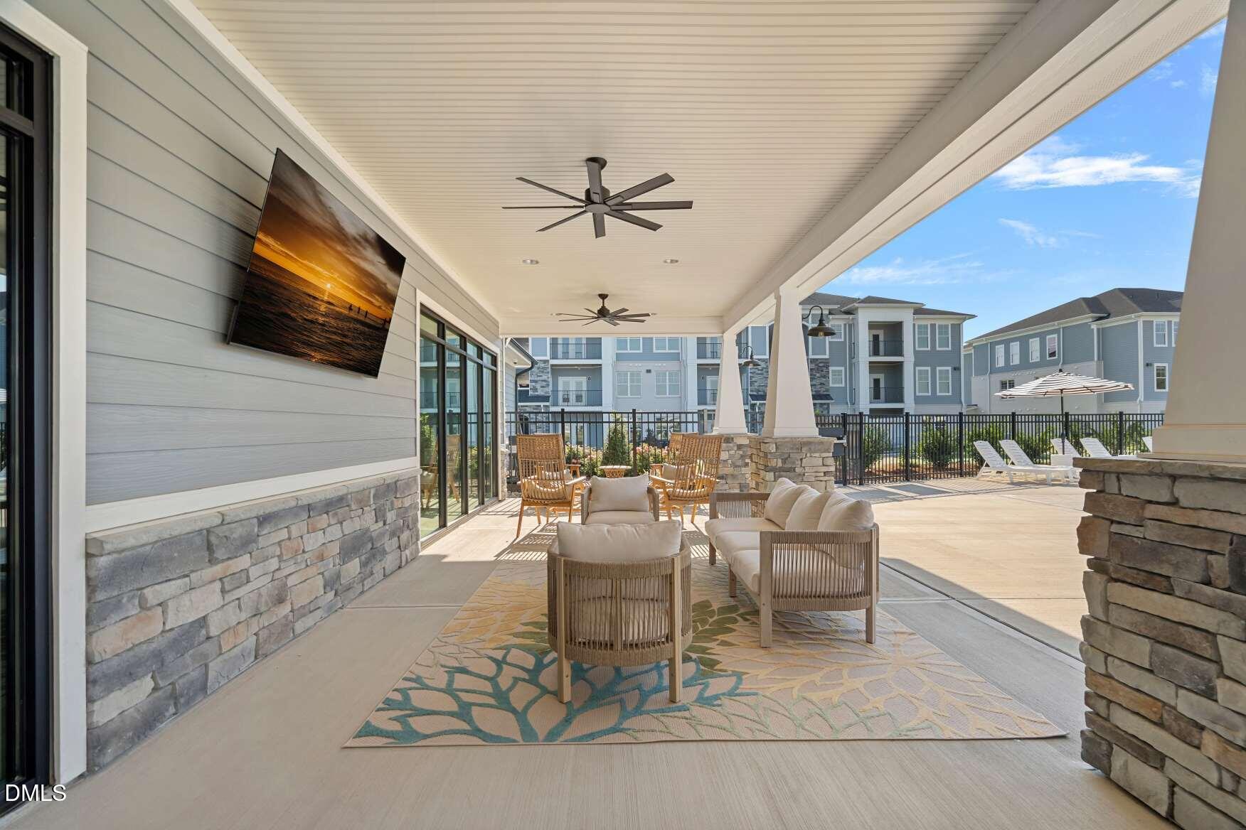 Covered patio with lounge seating, ceiling fans, stone accents, and views of neighboring townhomes.