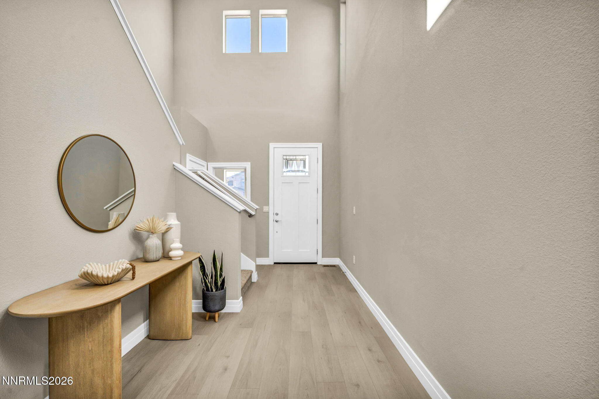 Entry foyer with a white front door, high windows, staircase, and curved wood console table.