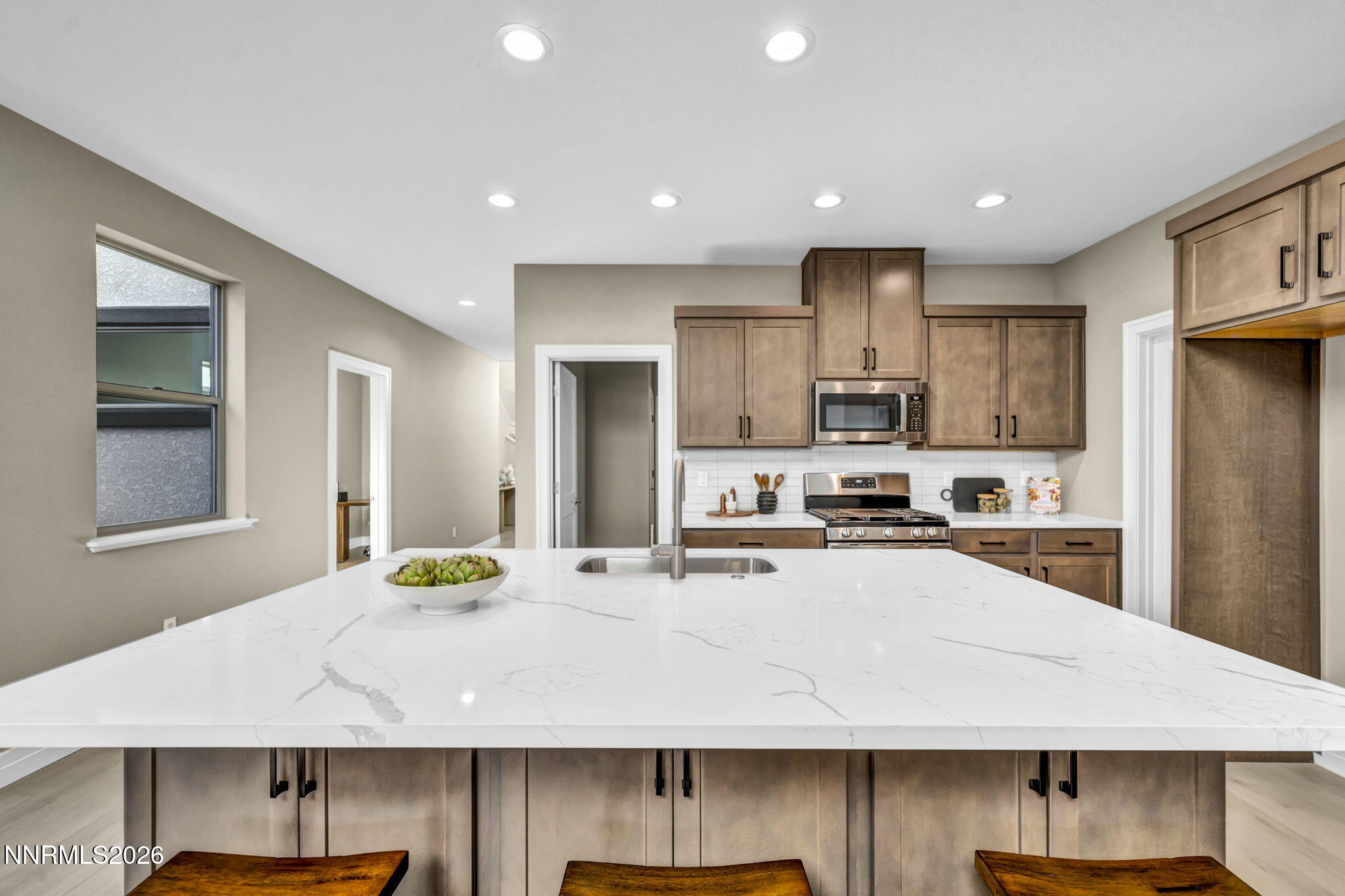 Kitchen with brown cabinets, stainless steel appliances, and a large white stone island.