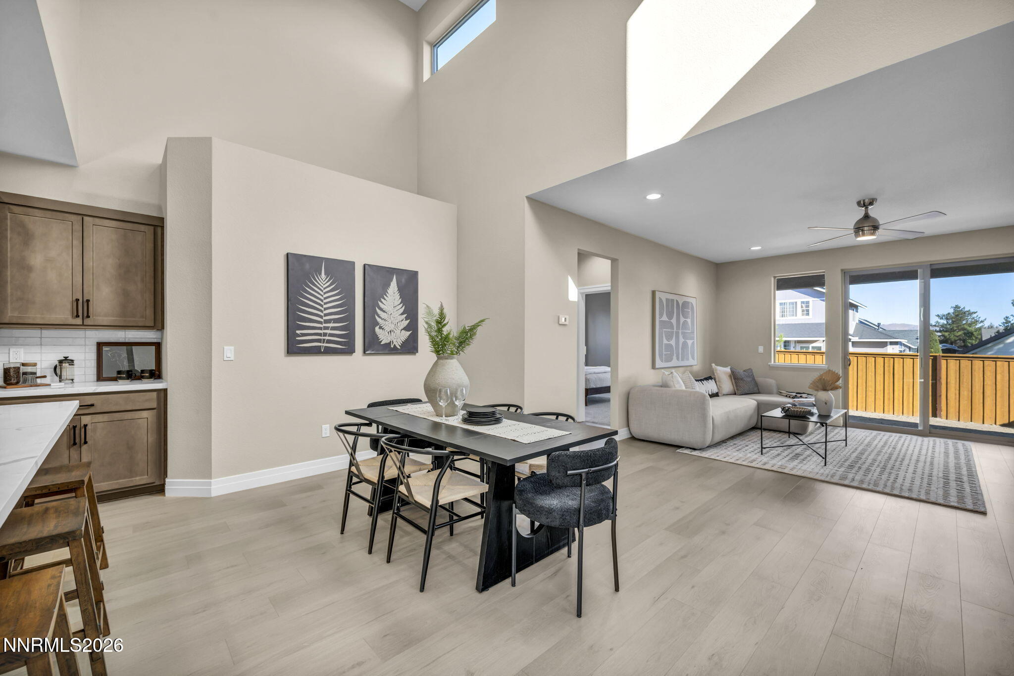 Open-plan living room, dining area, and kitchen with tall ceilings and sliding glass doors to a fenced patio.