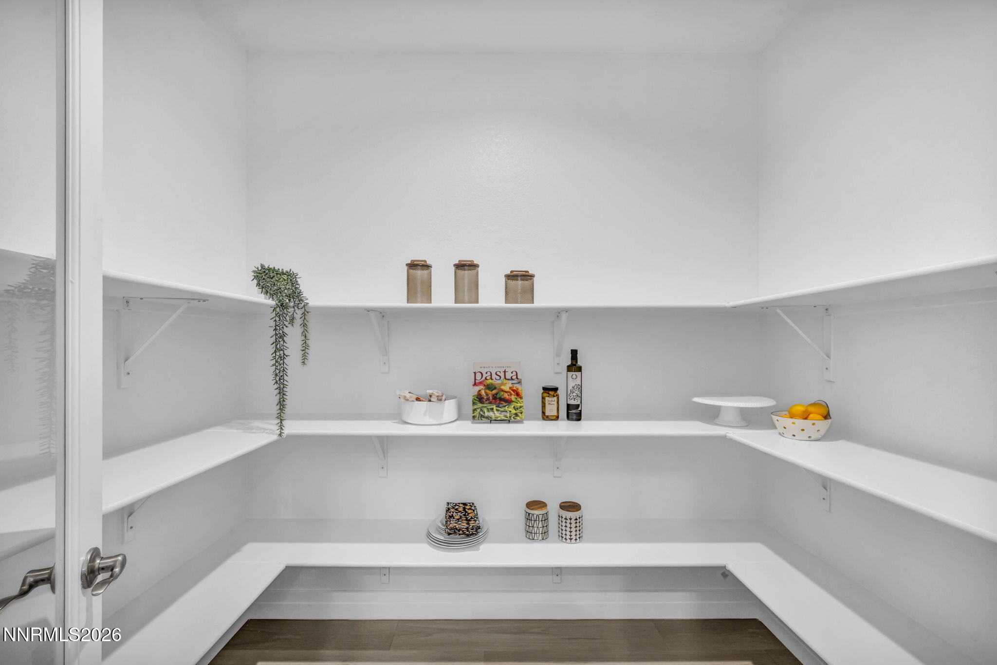 Walk-in pantry with white wraparound shelves and neatly arranged food and decor.