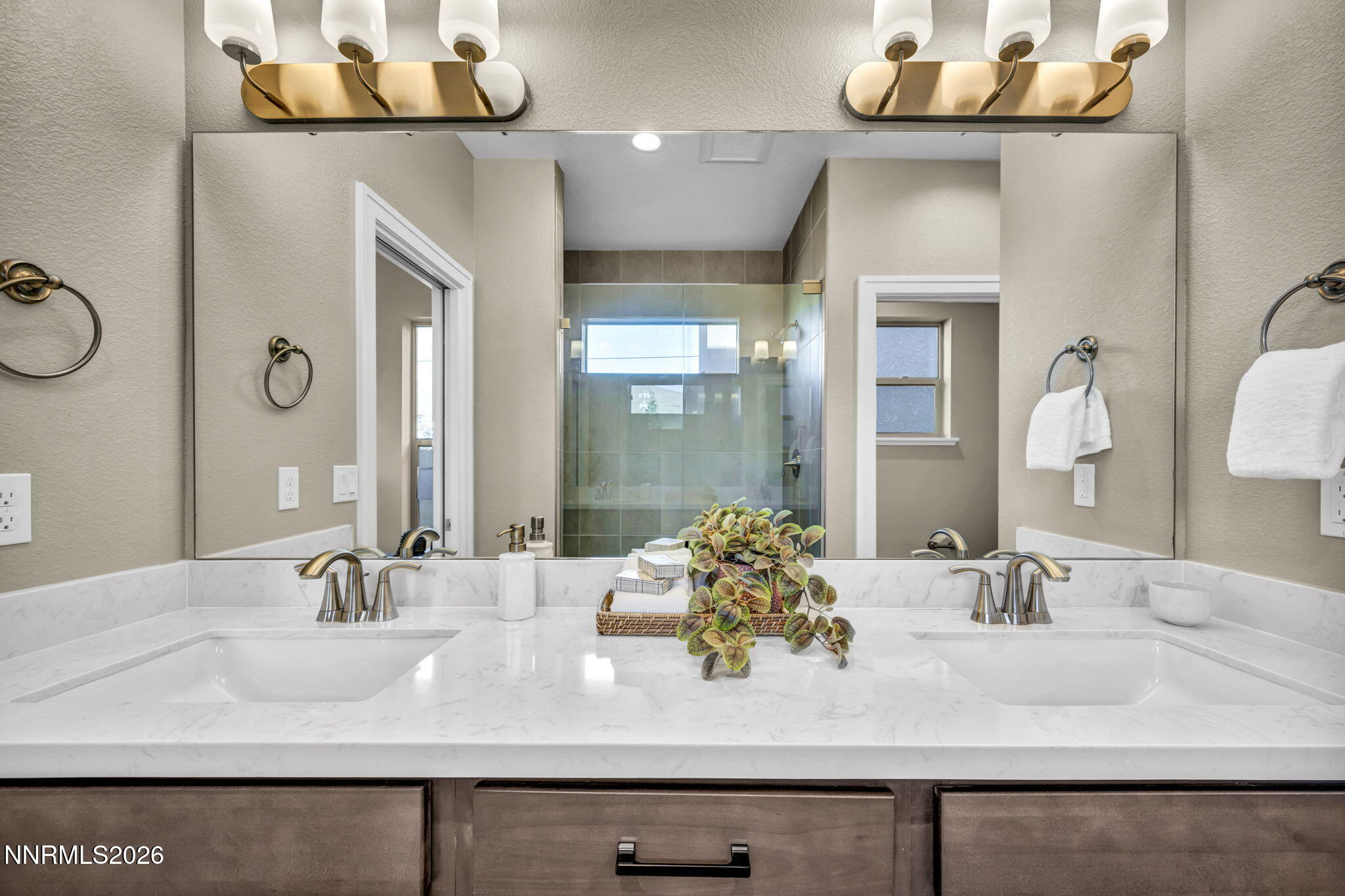 Bathroom with a double-sink marble-look vanity, brass fixtures, and a glass-enclosed tiled shower.