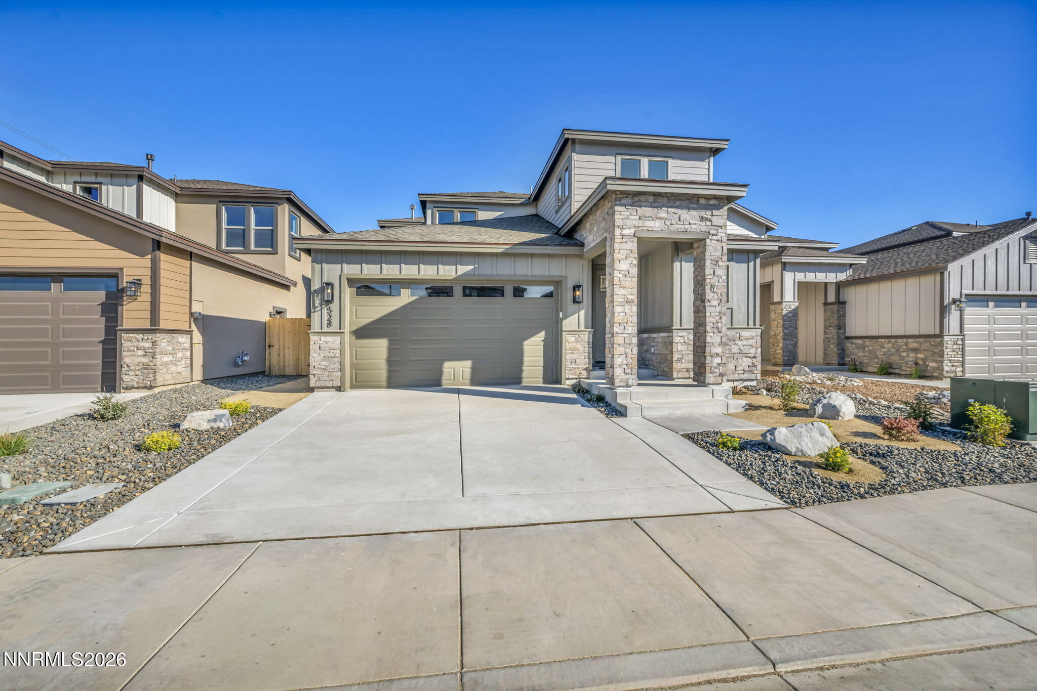 Modern two-story home with a stone entry surround, two-car garage, and broad concrete driveway.