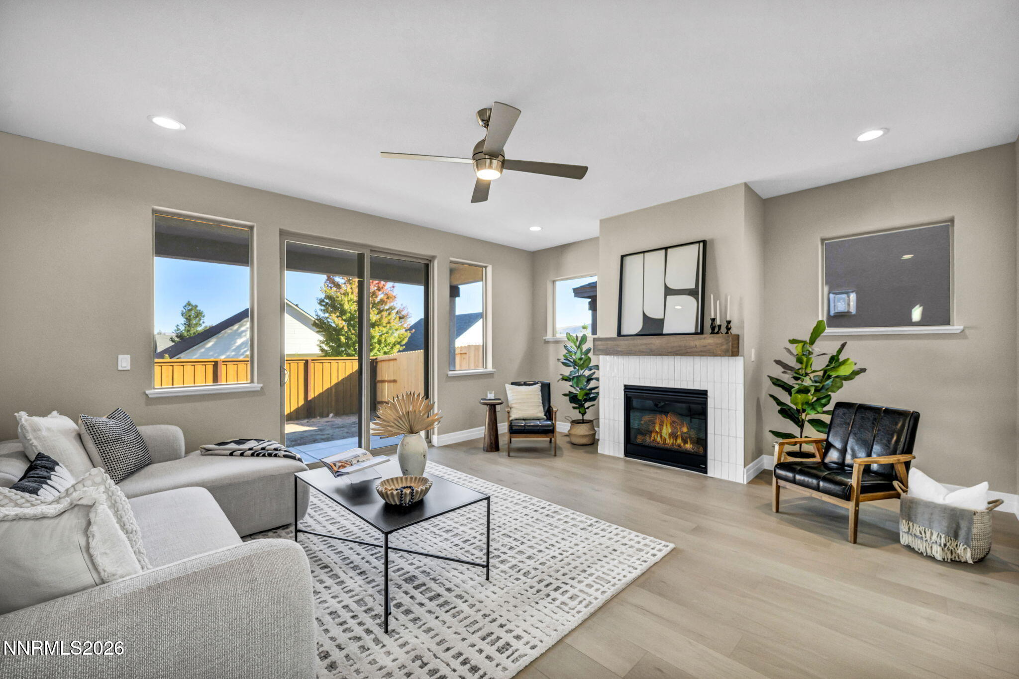 Living room with a tiled fireplace, gray sectional, and sliding glass doors to a fenced yard.