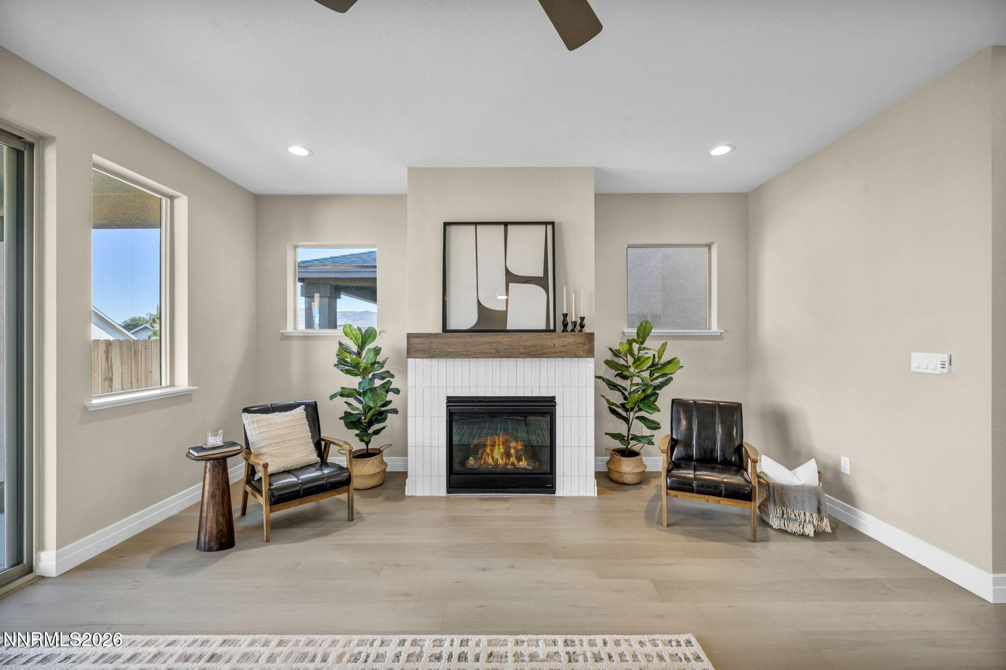 Staged living room with a tiled fireplace, wood mantel, and two black leather chairs.