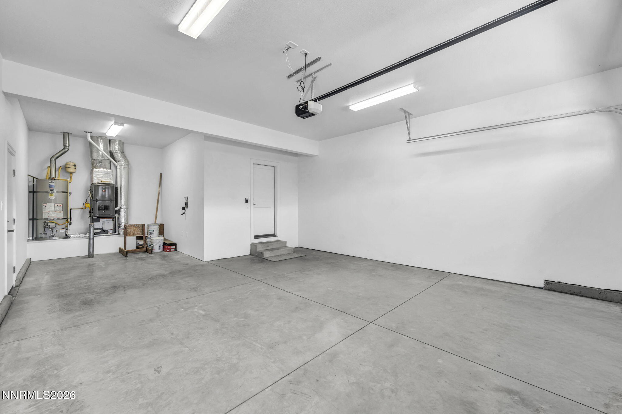 Empty garage with a concrete floor, overhead door opener, and utility equipment along one wall.