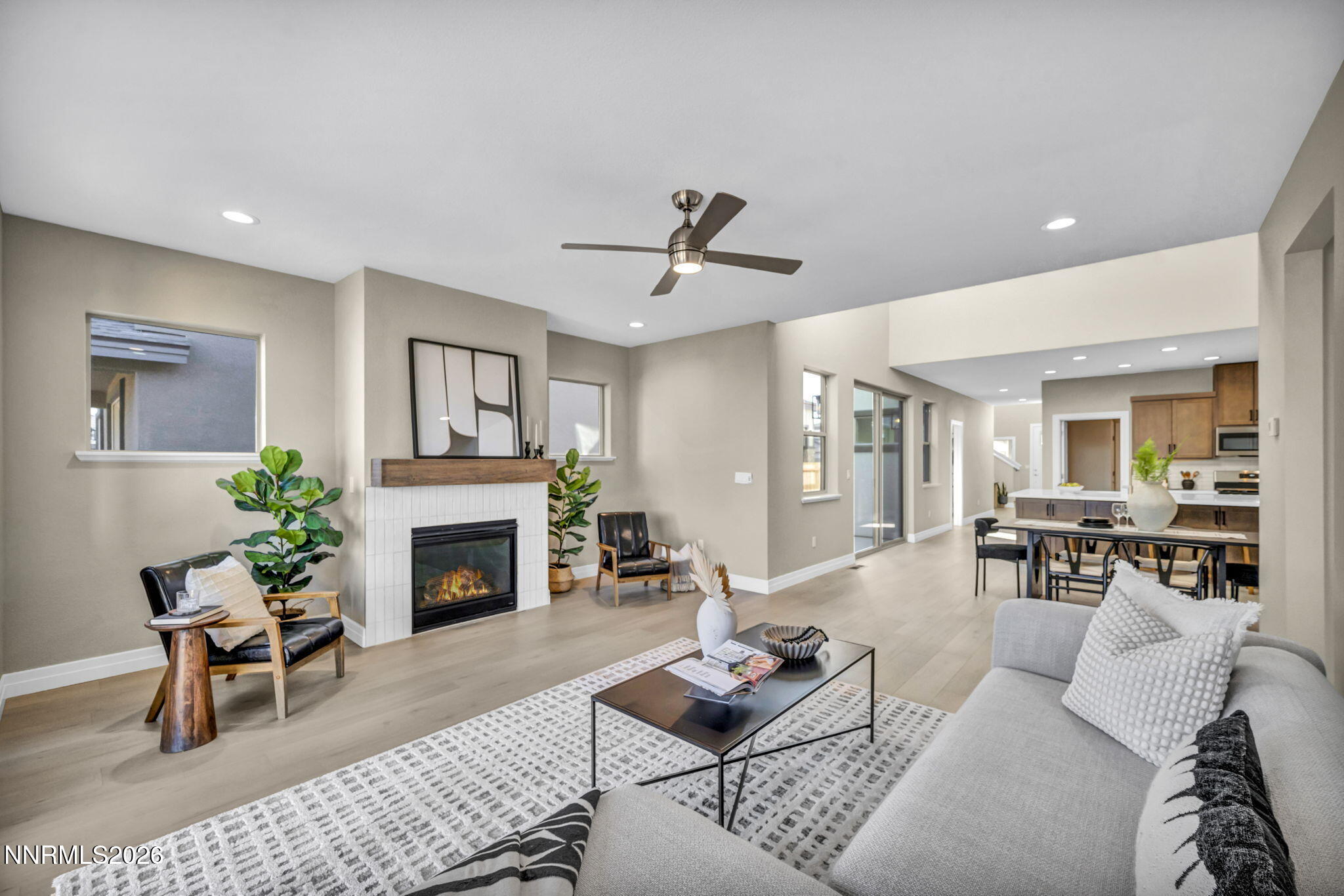 Open-plan living room with a white-tiled fireplace, gray sofa, and kitchen beyond.