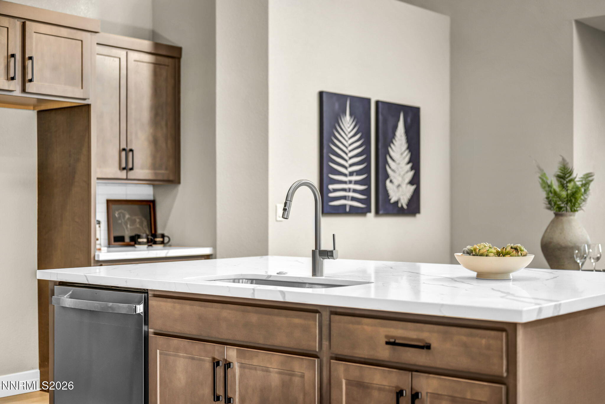 Kitchen island with white countertop, undermount sink, warm wood cabinetry, and stainless steel dishwasher.