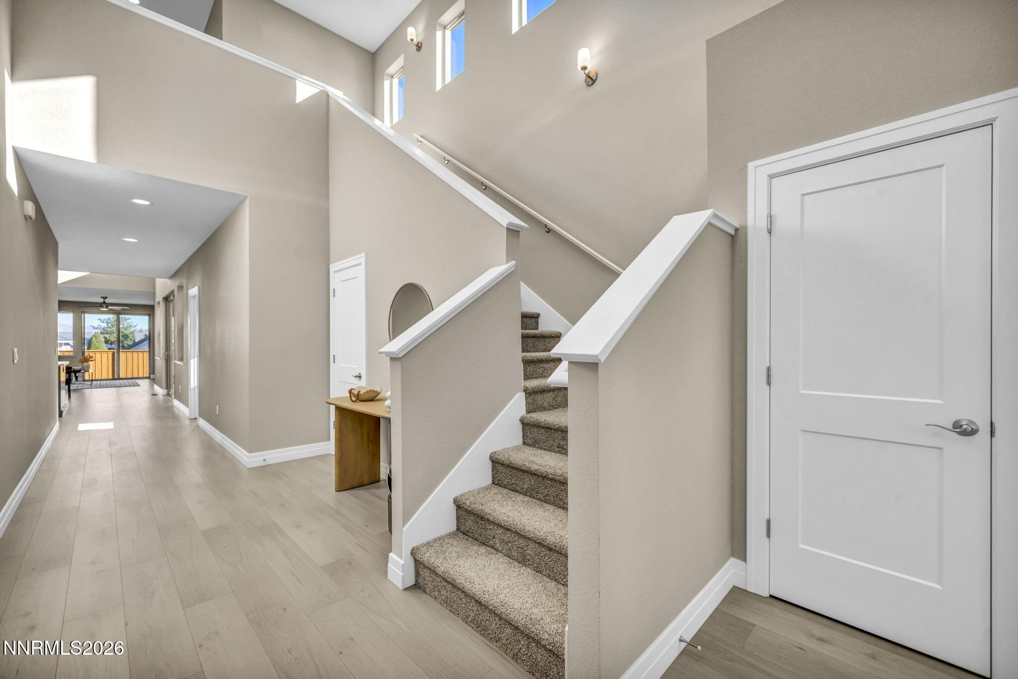 Two-story entryway with carpeted stairs and a long hallway leading to a balcony.