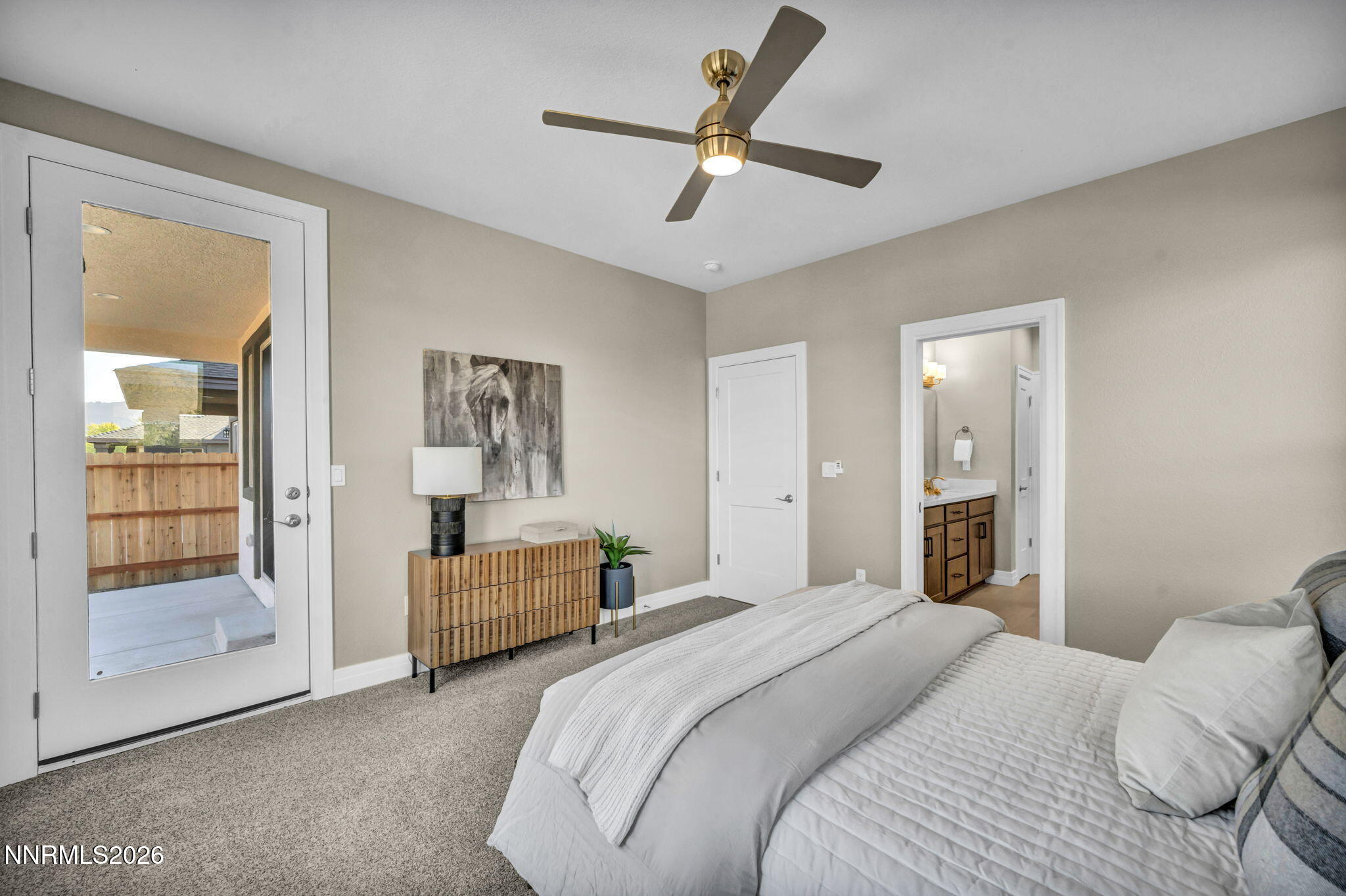 Bedroom with a glass patio door, ceiling fan, and bathroom vanity visible through the doorway.