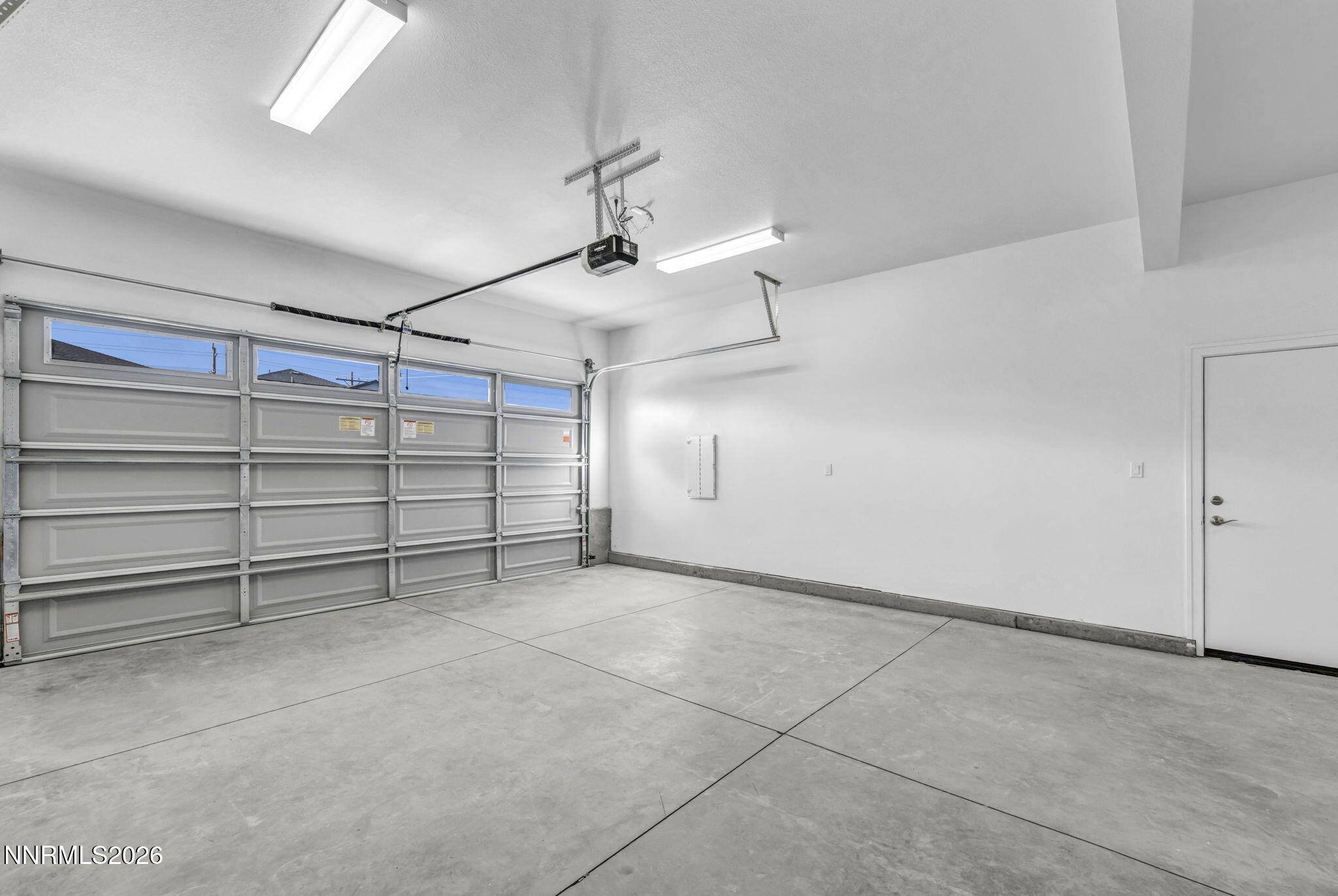 Empty garage with a concrete floor, large overhead door, and separate entry door.