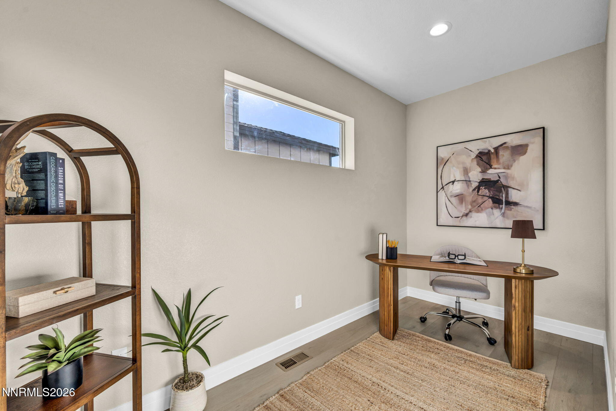 Staged home office with a wooden desk, arched shelving, and a high horizontal window.