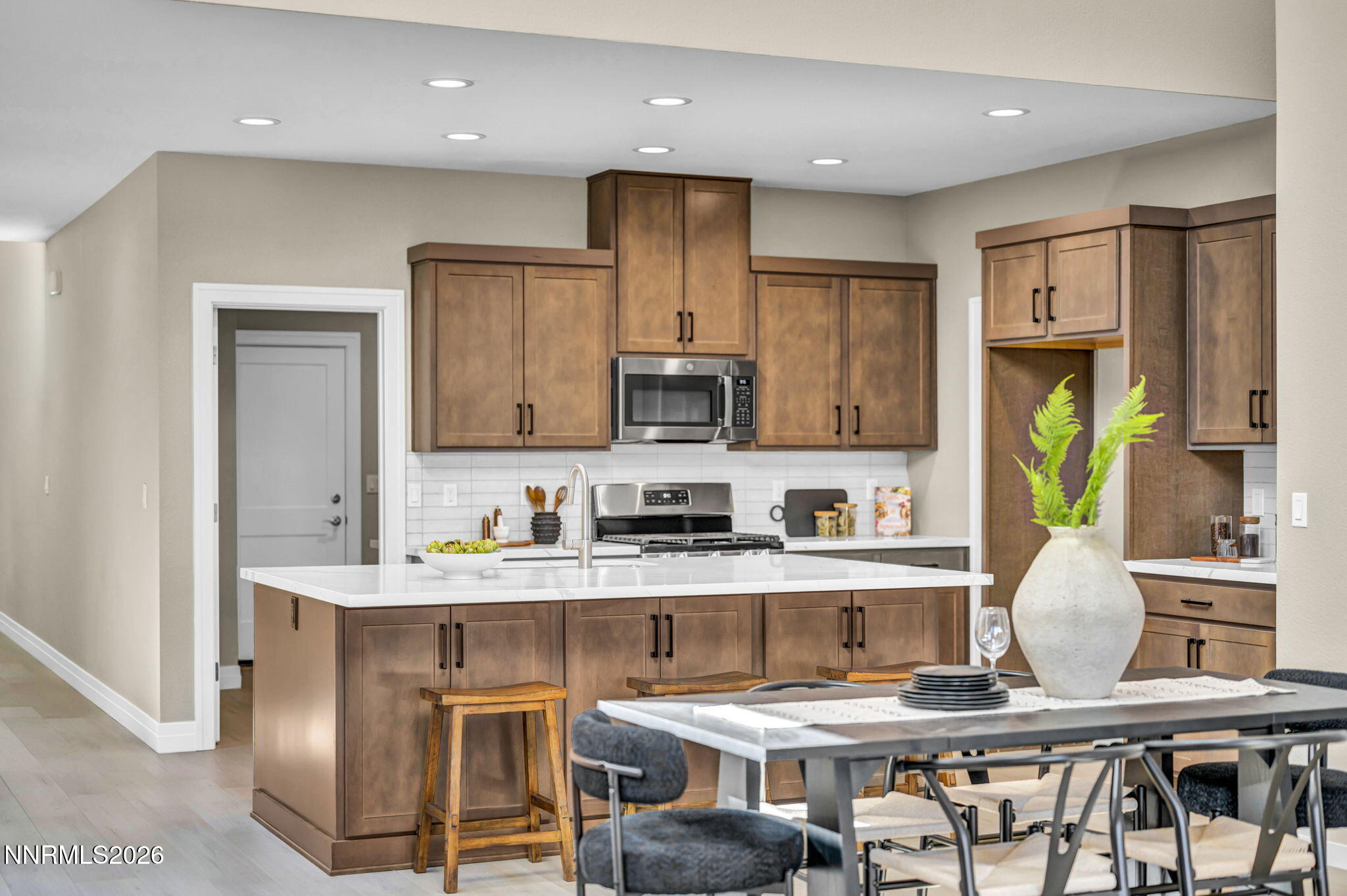Kitchen with brown cabinets, stainless appliances, and a white island beside a dining table.