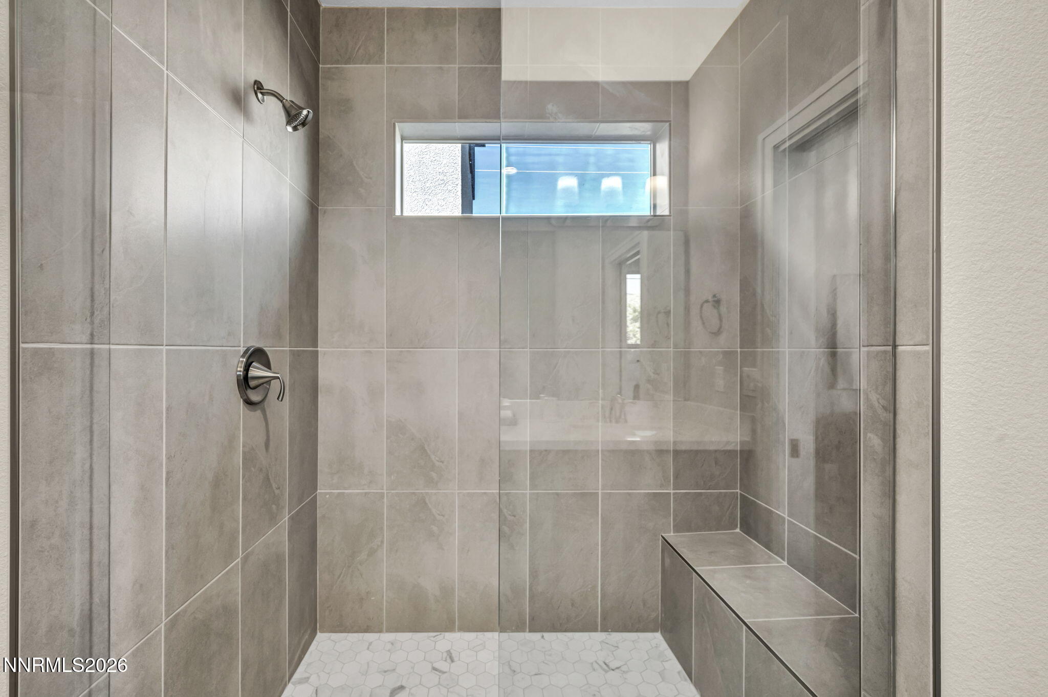 Walk-in shower with gray tile walls, a glass enclosure, built-in bench, and high horizontal window.