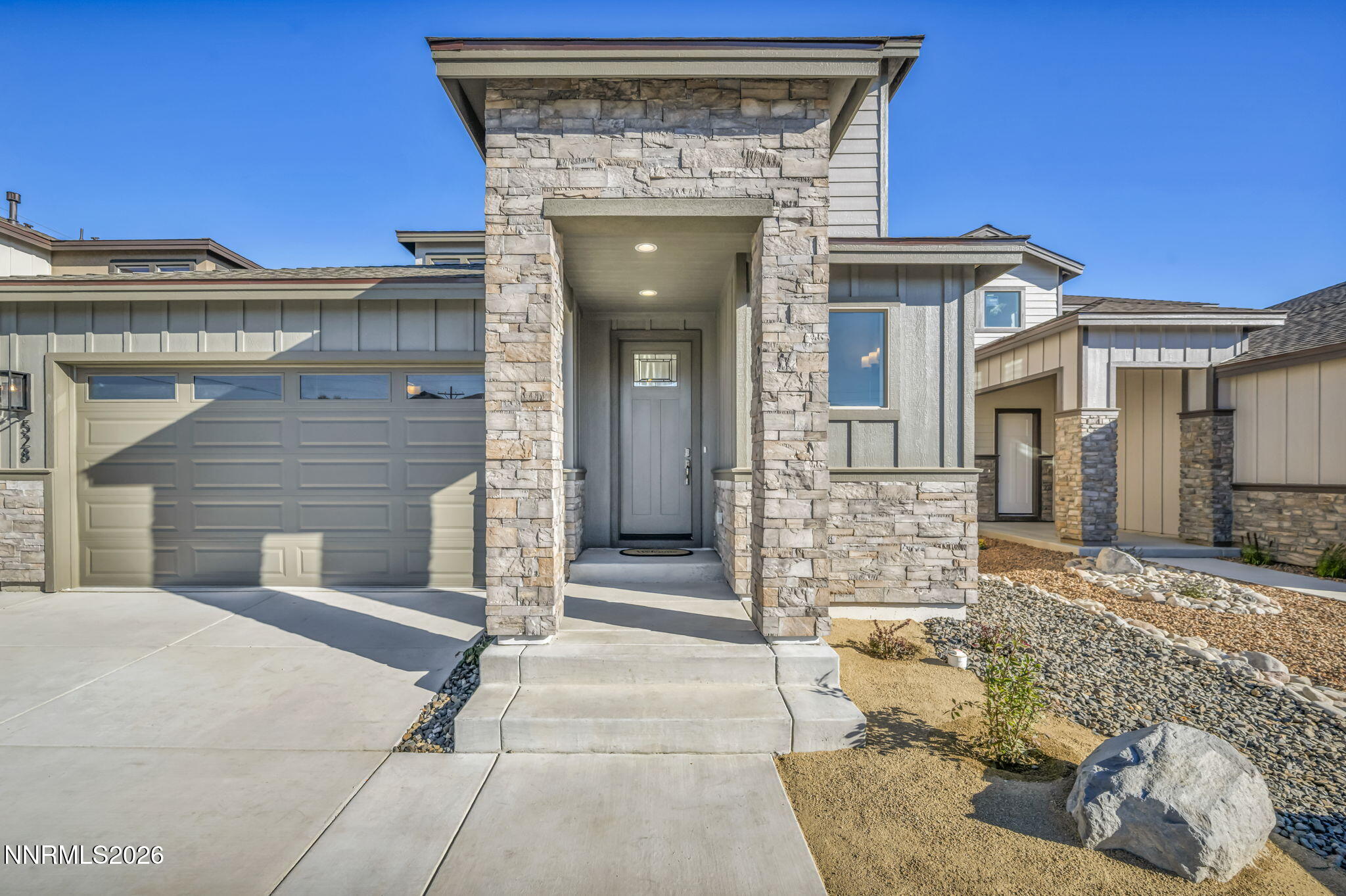 Modern home exterior with a stone-framed entry, attached garage, and gravel landscaping.