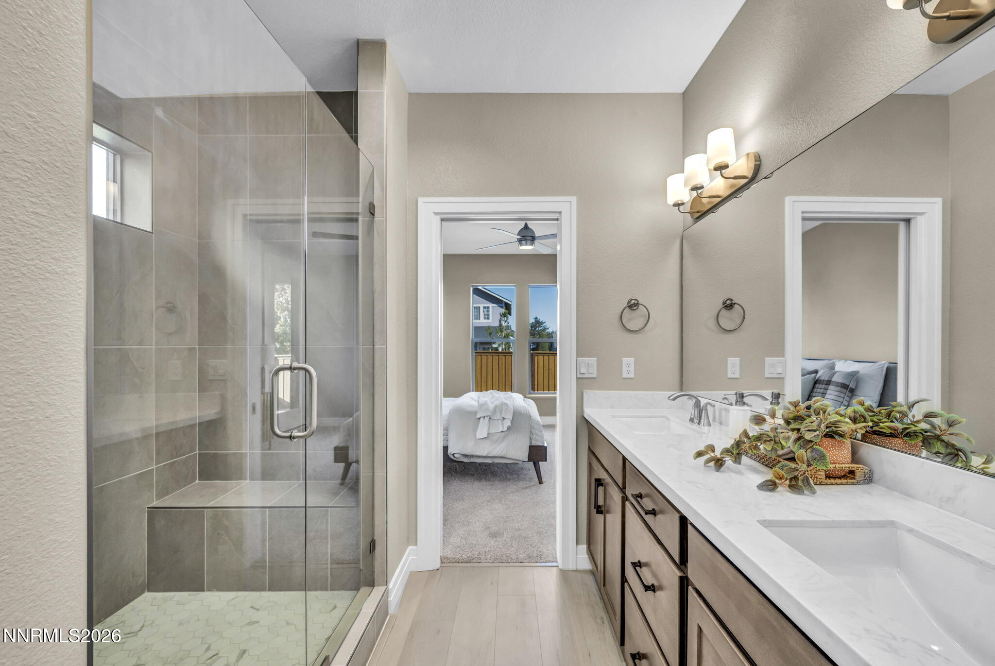 Bathroom with a glass-enclosed tiled shower, double-sink vanity, and doorway to a bedroom.