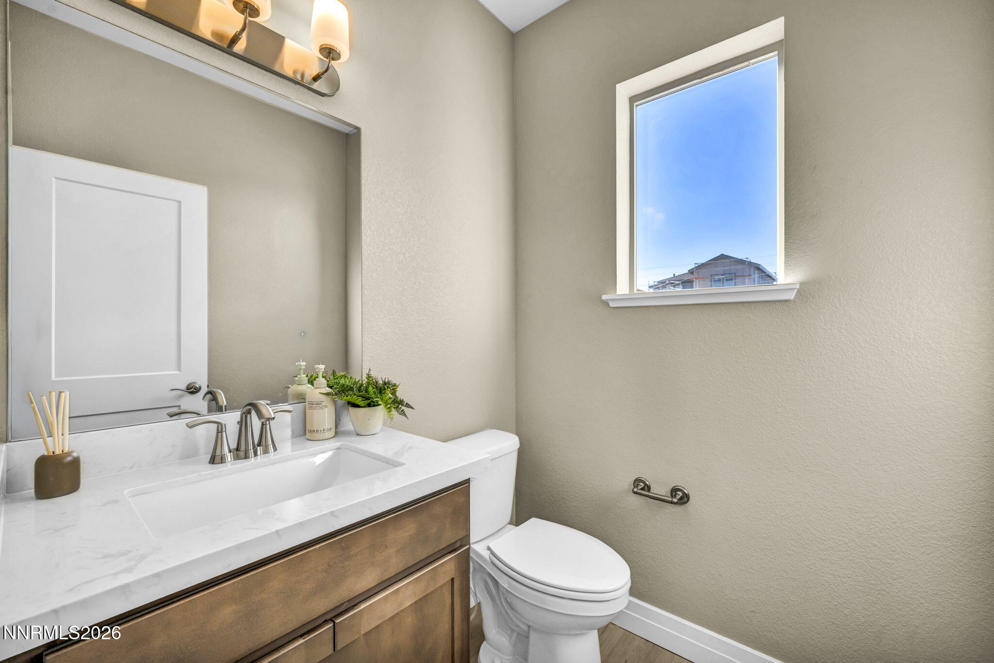 Bathroom with a marble-look vanity, wood-tone drawers, white toilet, and high window.