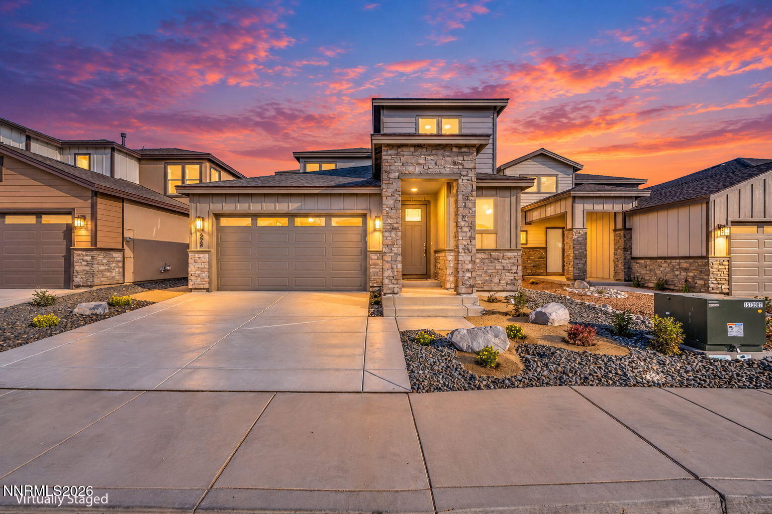 Modern two-story home with stone accents and a double garage beneath a vivid sunset.