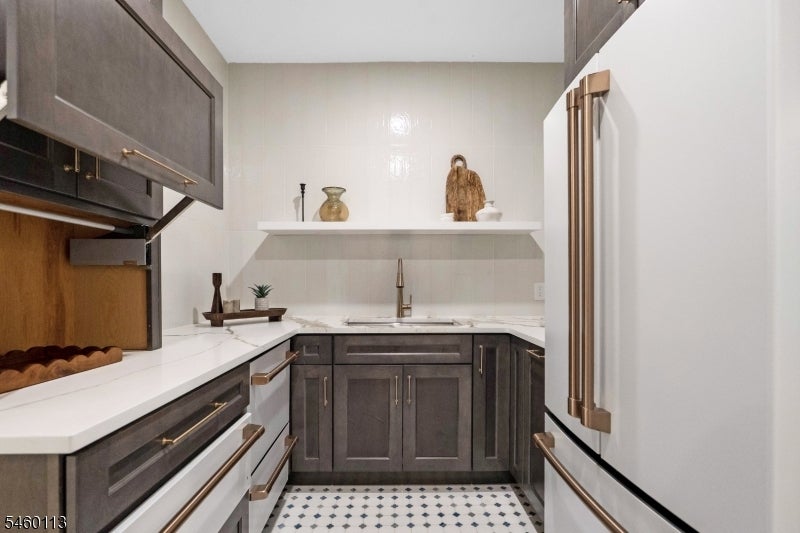 Kitchen with dark gray cabinets, brass hardware, white counters, and patterned tile flooring.