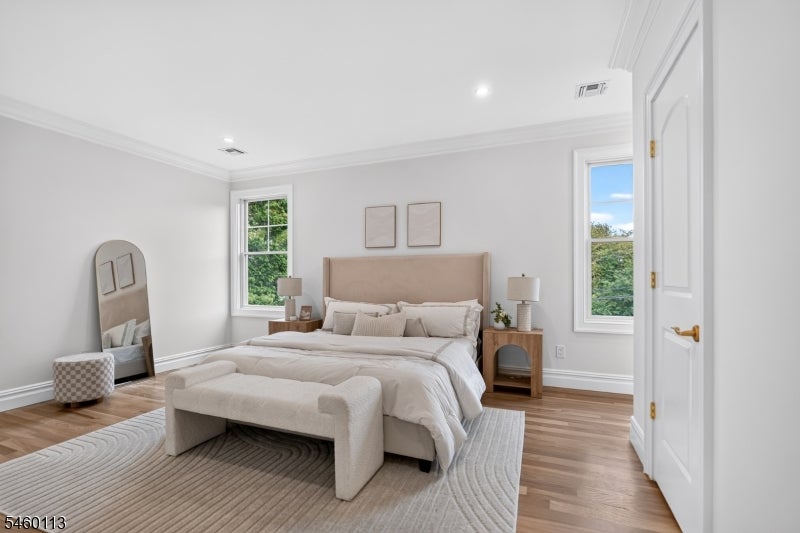 Staged bedroom with a king bed, upholstered bench, hardwood floors, and windows overlooking trees.