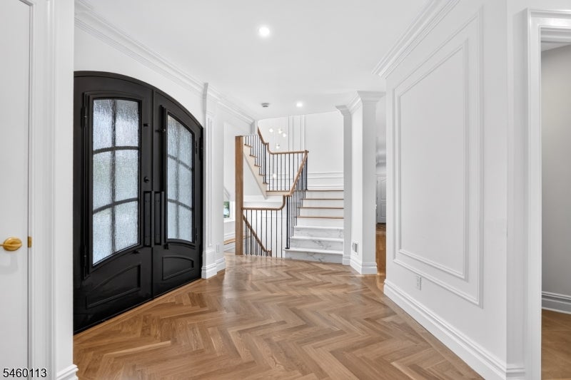 Entry foyer with black arched doors, herringbone flooring, and a marble staircase.