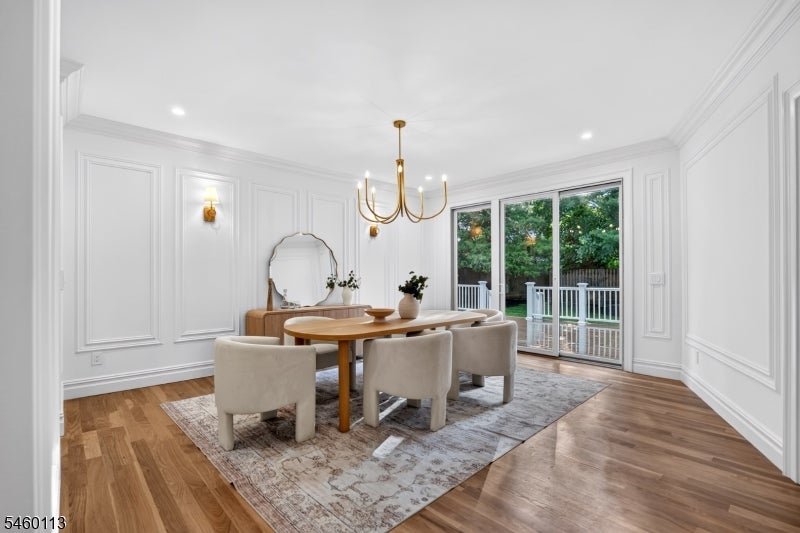 Dining room with white paneled walls, a wood table, gold chandelier, and garden-facing glass doors.