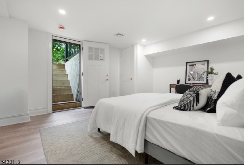 Furnished bedroom with a white bed beside a glass door opening onto exterior steps.