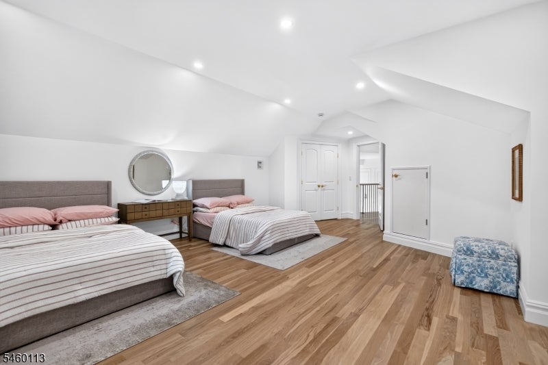 Bedroom with two beds, striped bedding, hardwood floors, and a round mirror above the shared nightstand.