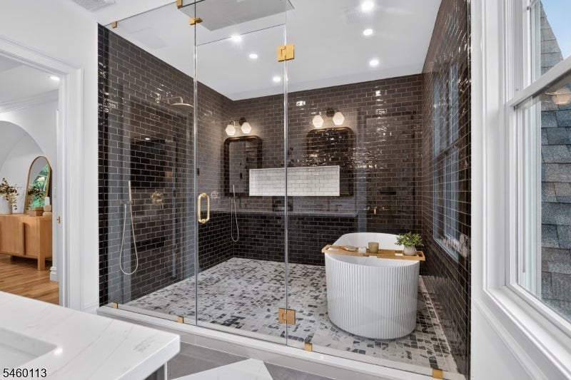Bathroom with a glass-enclosed dark-tile shower, mosaic floor, and freestanding white tub.