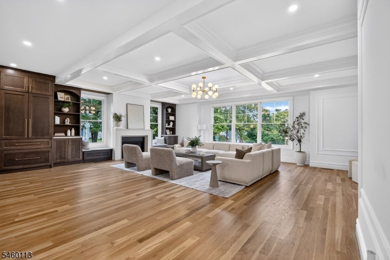 Living room with a coffered ceiling, fireplace, built-ins, and large windows overlooking trees.