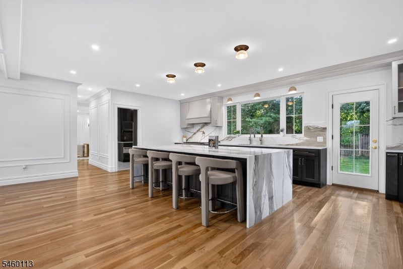 Renovated kitchen with a marble-look waterfall island, five stools, dark lower cabinets, and hardwood floors.