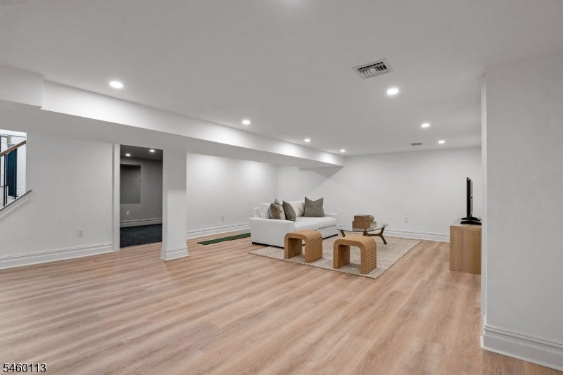 Furnished living area with a white sectional, woven stools, and light wood flooring.