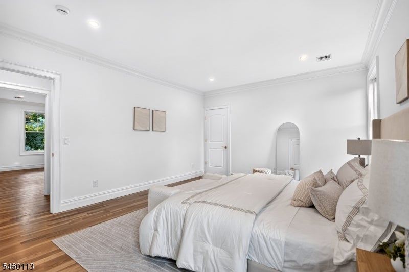 Bright bedroom with white bedding, hardwood floors, and an arched mirror.