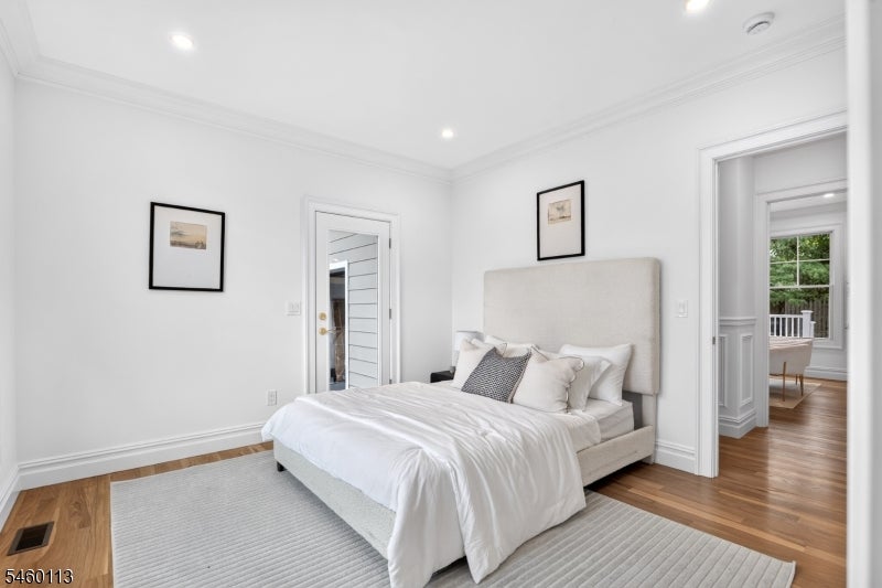 Staged bedroom with a white bed, upholstered headboard, gray rug, and hardwood floors.