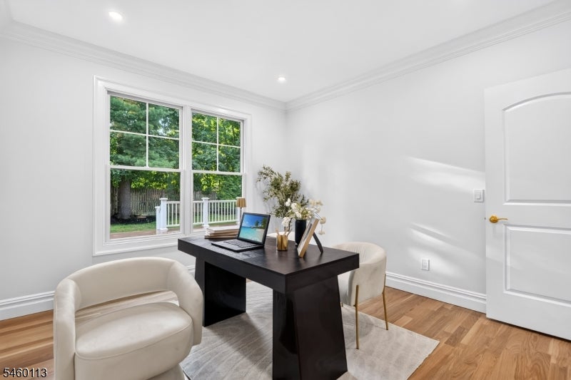 Staged home office with a dark desk and cream chairs beside a large window overlooking a fenced yard.