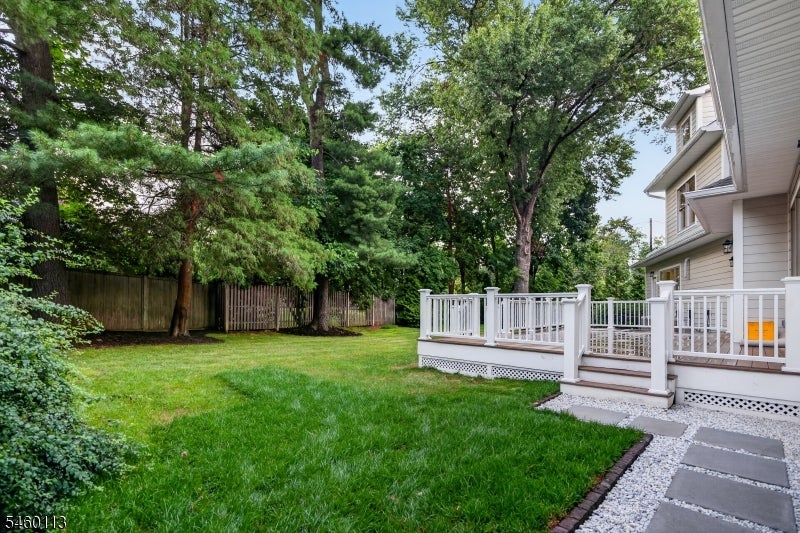 Backyard lawn and mature trees beside a white-railed deck and stone walkway.
