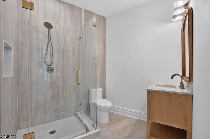 Modern bathroom with a tiled glass shower, white toilet, and wood vanity beneath an arched mirror.