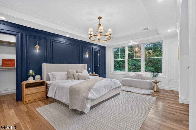 Staged bedroom with a navy paneled wall, white bed, chandelier, and window-side sitting area.