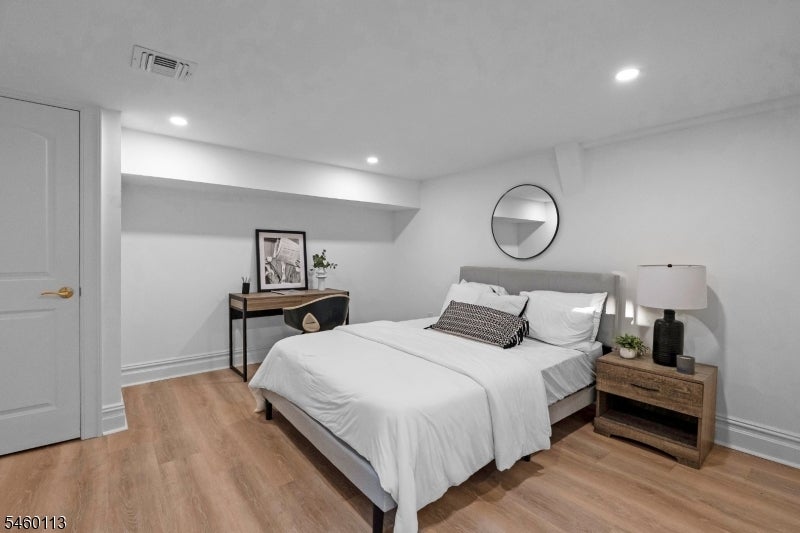 Staged bedroom with a white bed, round wall mirror, and wood nightstand.