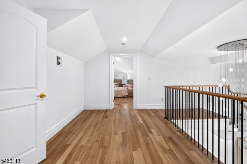 Upstairs landing with wide-plank wood floors, black stair railing, and a bedroom beyond the doorway.