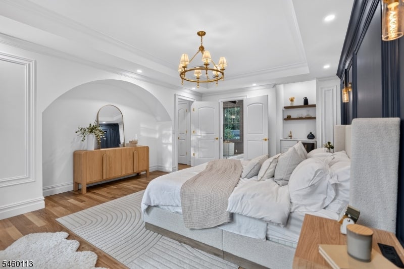 Bedroom with a white bed, gold chandelier, arched alcove, and dark blue accent wall.