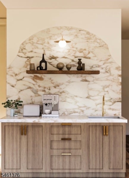 Kitchen coffee station with an arched marble backsplash, light wood cabinets, and brass faucet.