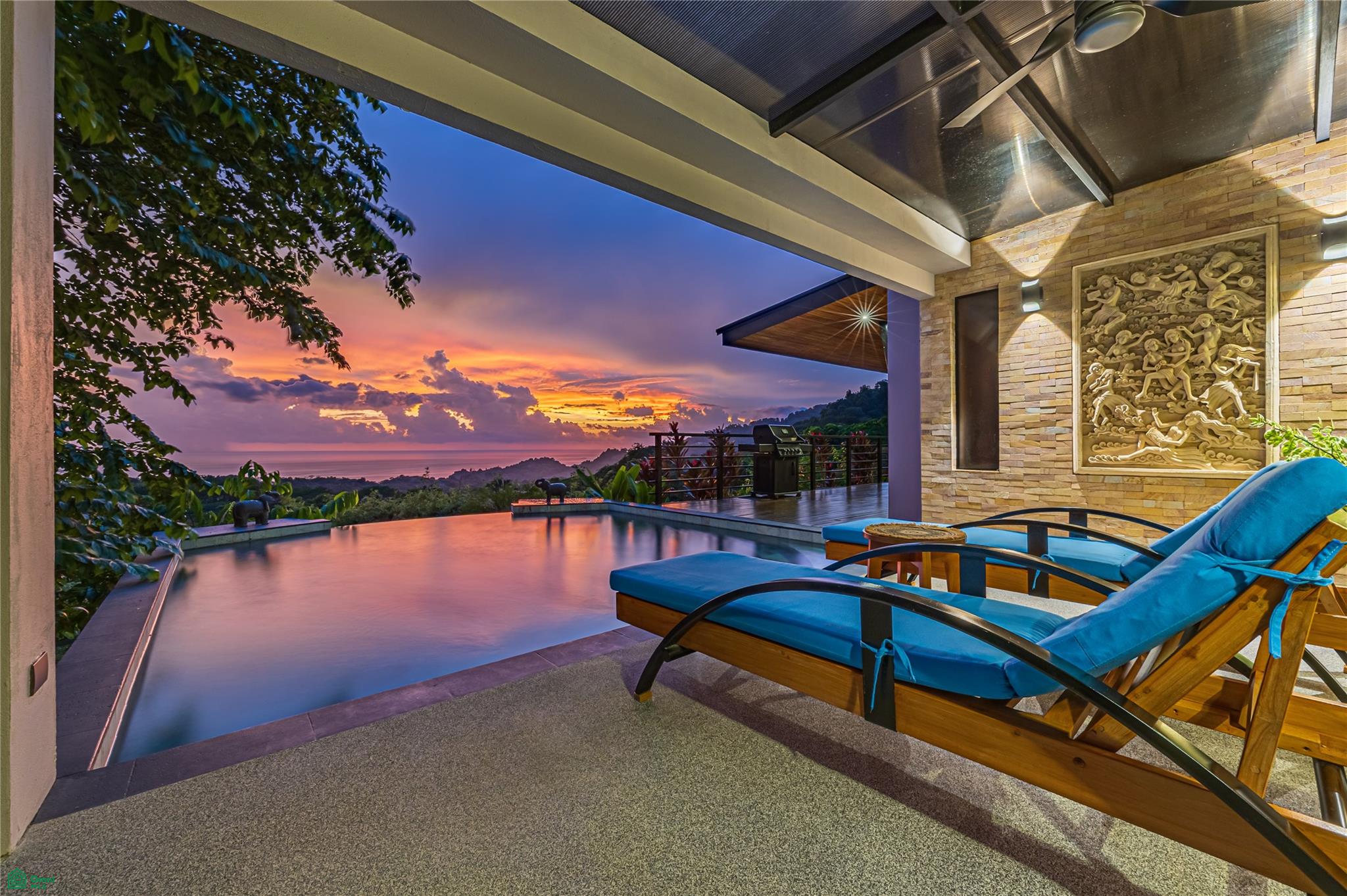 Infinity pool terrace with blue loungers overlooks the ocean at sunset.