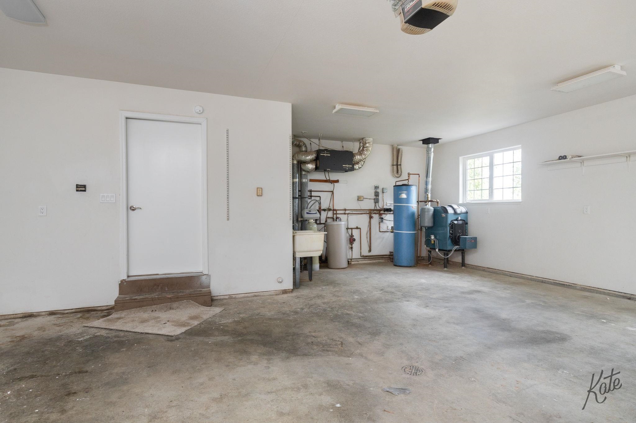 Garage utility area with a concrete floor, utility sink, blue water heater, and boiler.