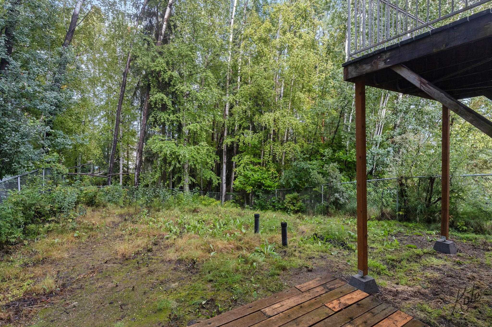 Wooded backyard with a raised deck, chain-link fence, and mature trees.