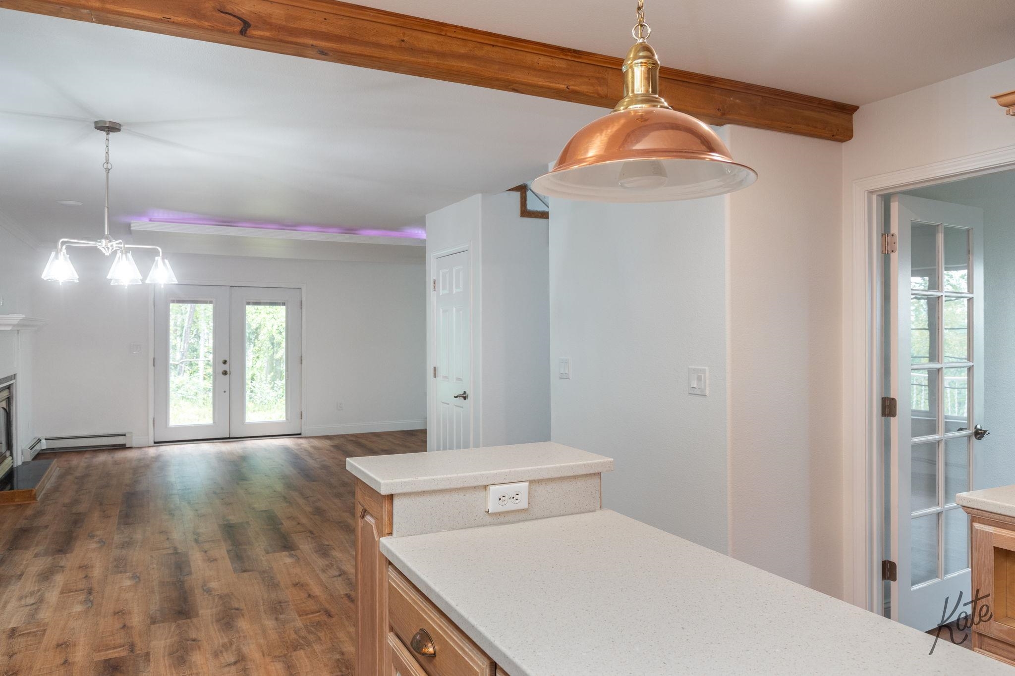 Open kitchen and dining area with white counters, wood floors, and exposed ceiling beams.