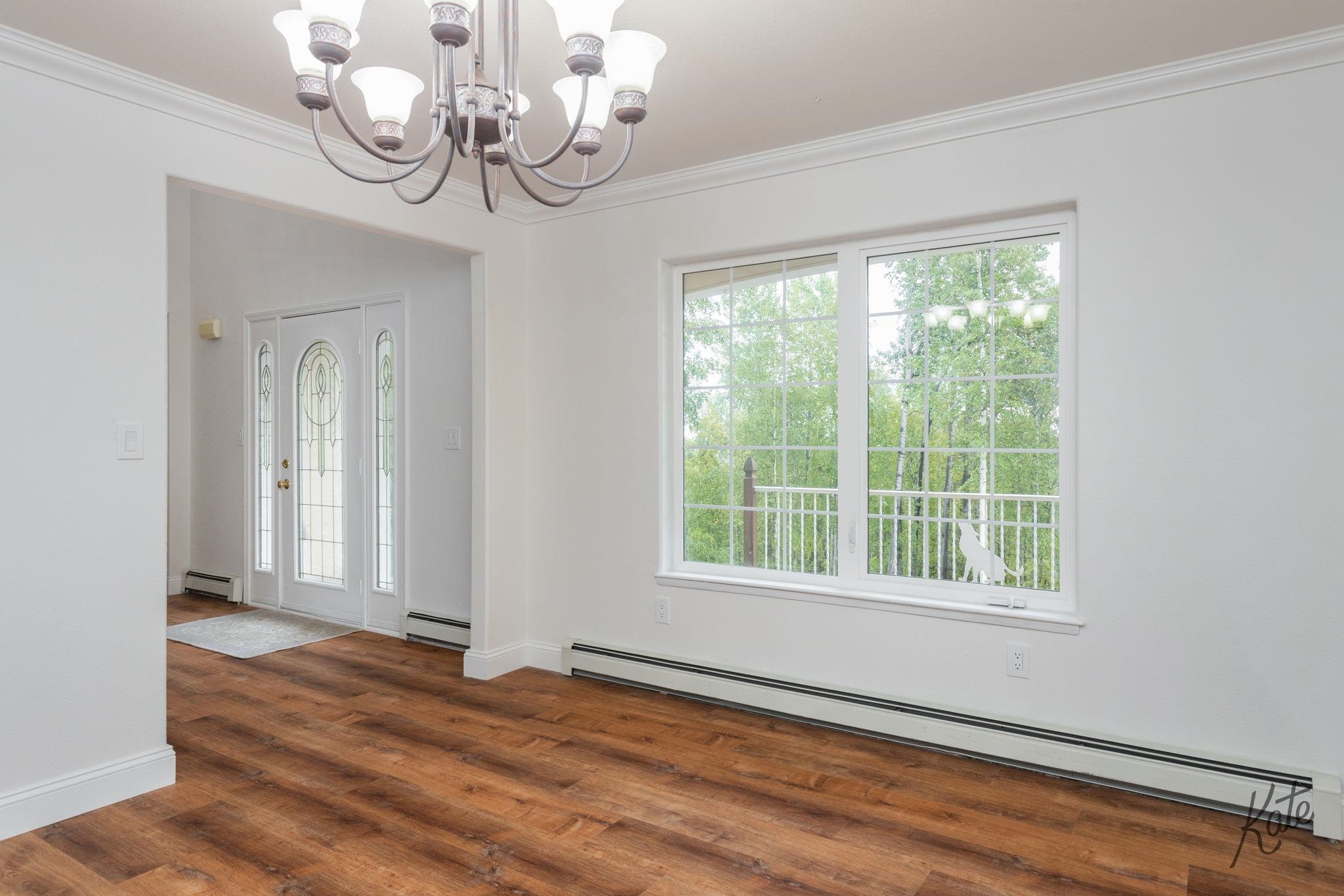 Empty entry area with hardwood floors, a glass-paneled front door, chandelier, and large leafy-view window.